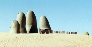 Statue of  4 fingers and a thumb coming out of the sand